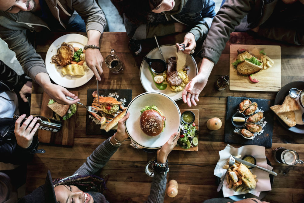 View from above of a laid table with food. A group of people are sitting around the table and starting to eat.