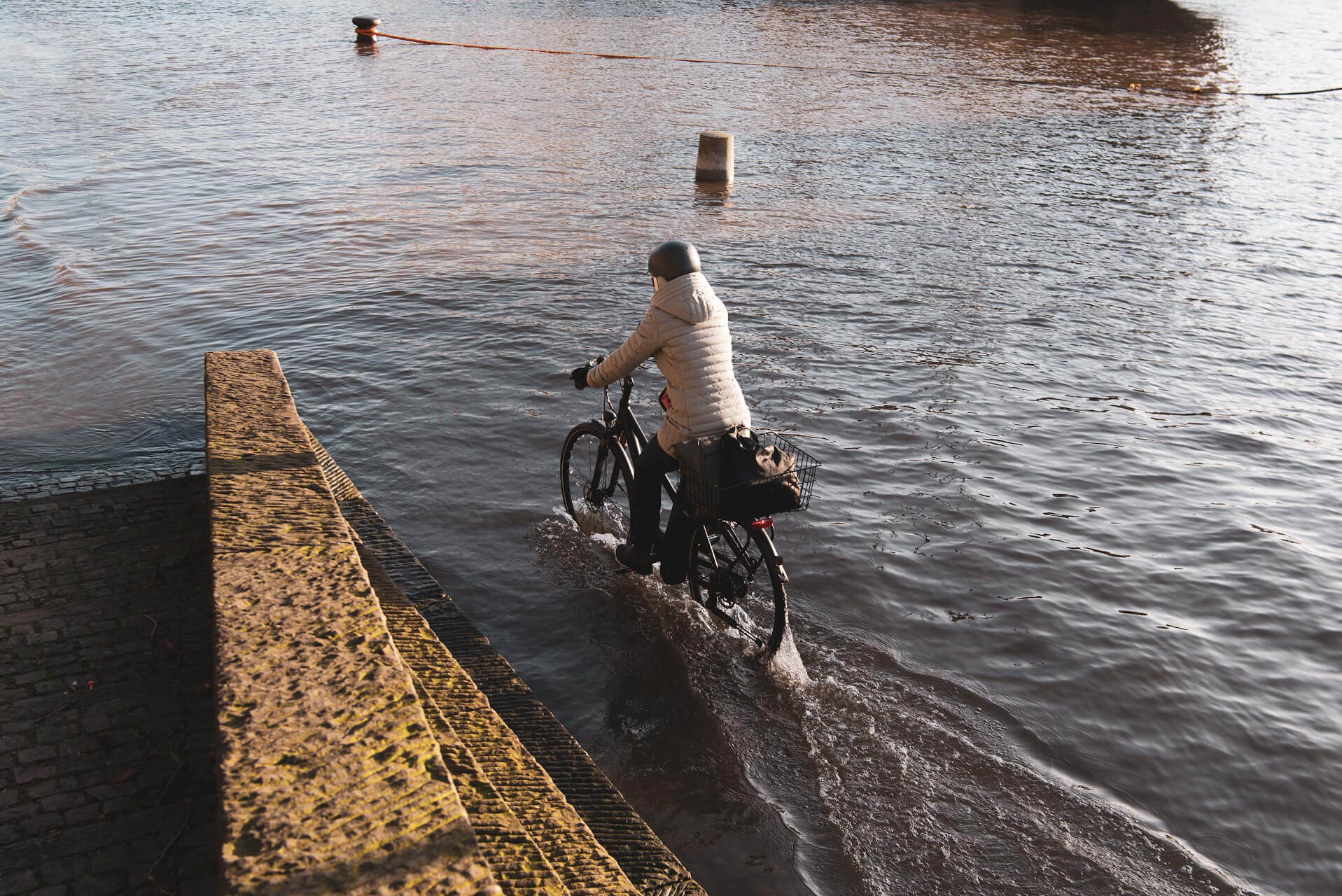 Radfahrerin in Bremen fährt am überfluteten Fluss Weser