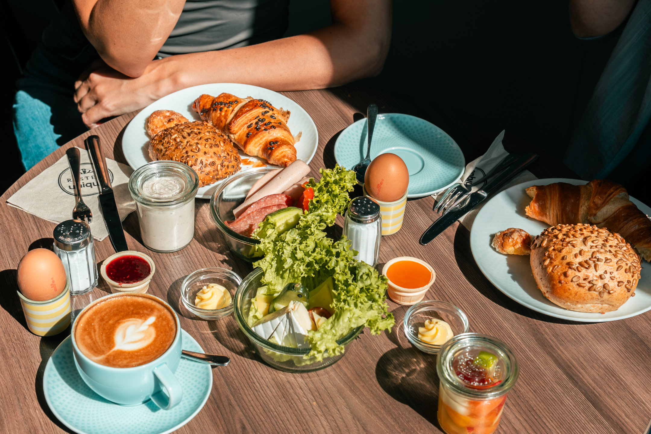 Voll gedeckter Frühstückstisch mit Gebäck, Aufschnitt, Eiern, Obst und Kaffee.