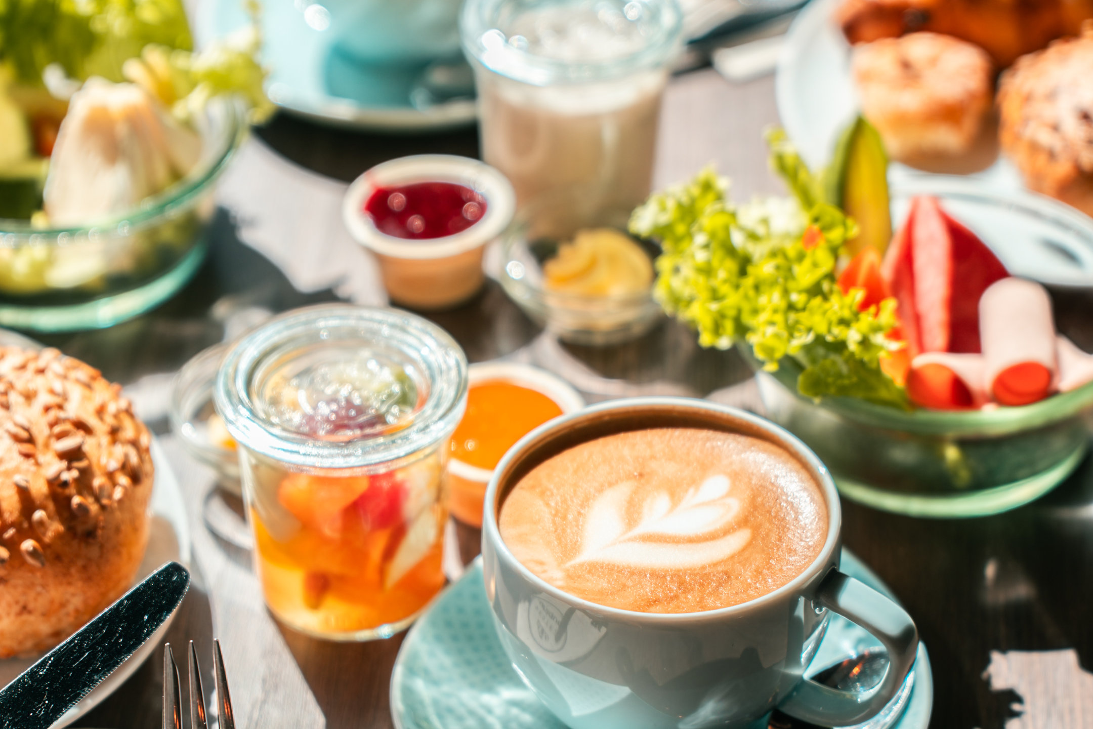 Ein voll gedeckter Frühstückstisch mit Obstsalat, Cappuccino, Wurst und Brötchen