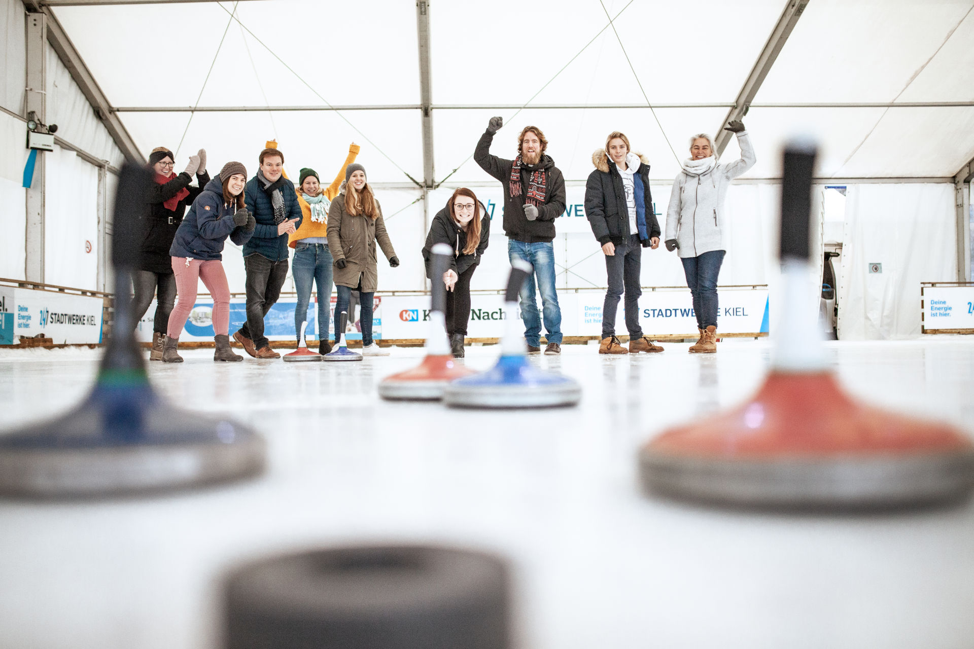 Gruppe beim Eisstockschießen in einer überdachten Halle, lachend und jubelnd, im unique by ATLANTIC Hotels Kiel.