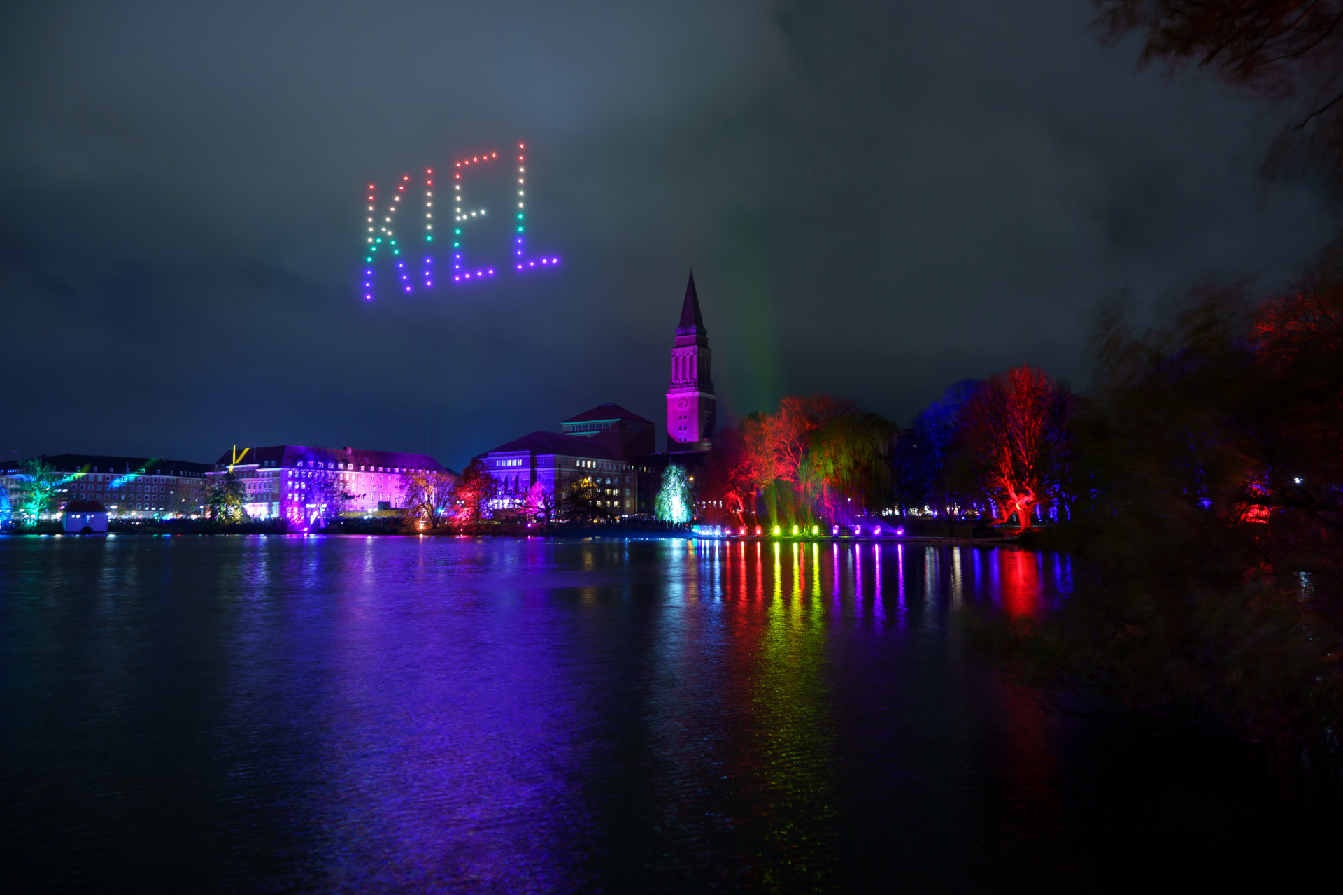 Lichtermeer in Kiel | unique by ATLANTIC Hotels Kiel Bunte Lichtershow über Kieler Skyline bei Nacht, reflektiert im Wasser.